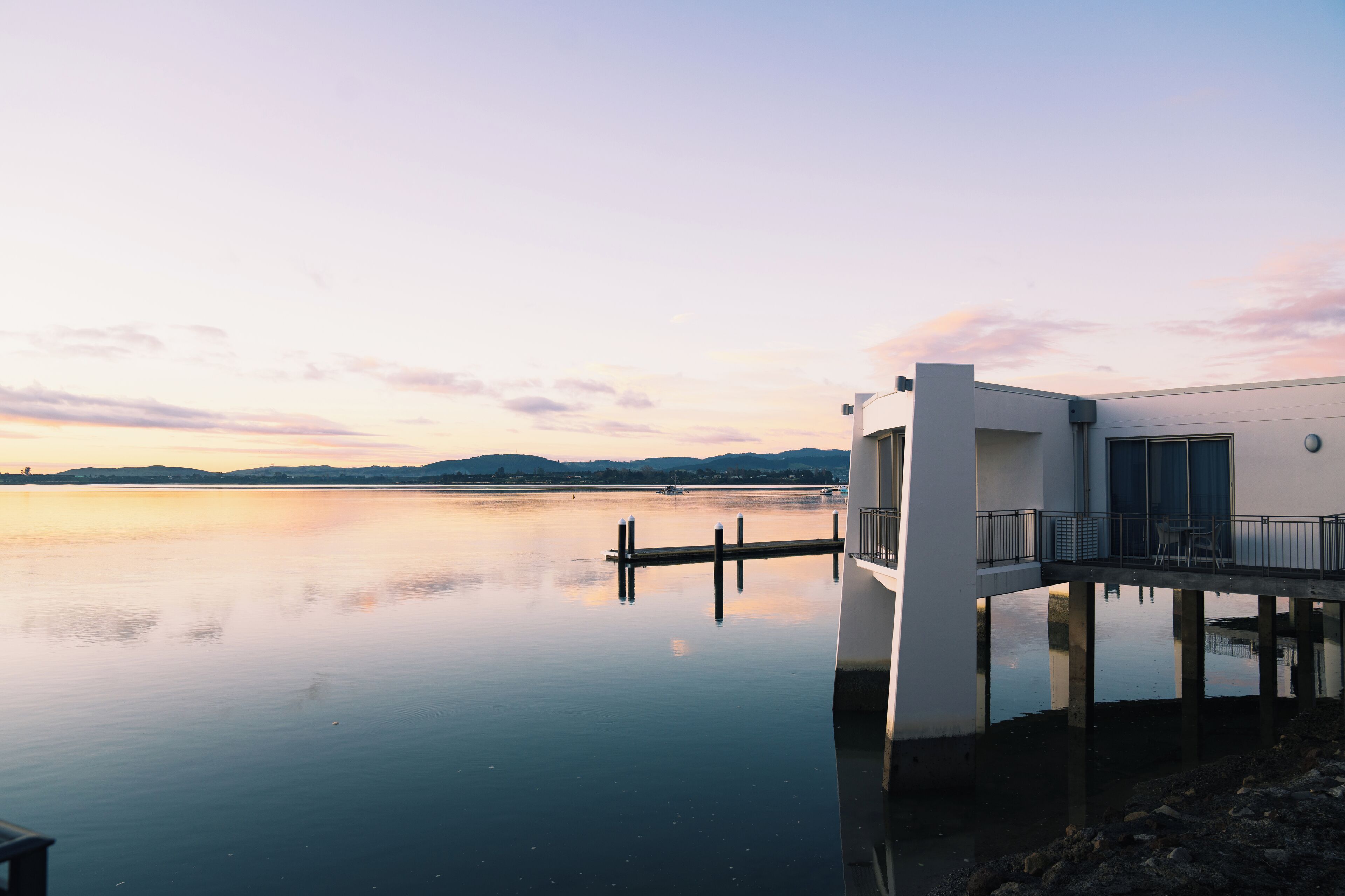 A modern building with a dock extending into calm water, surrounded by mountains.
