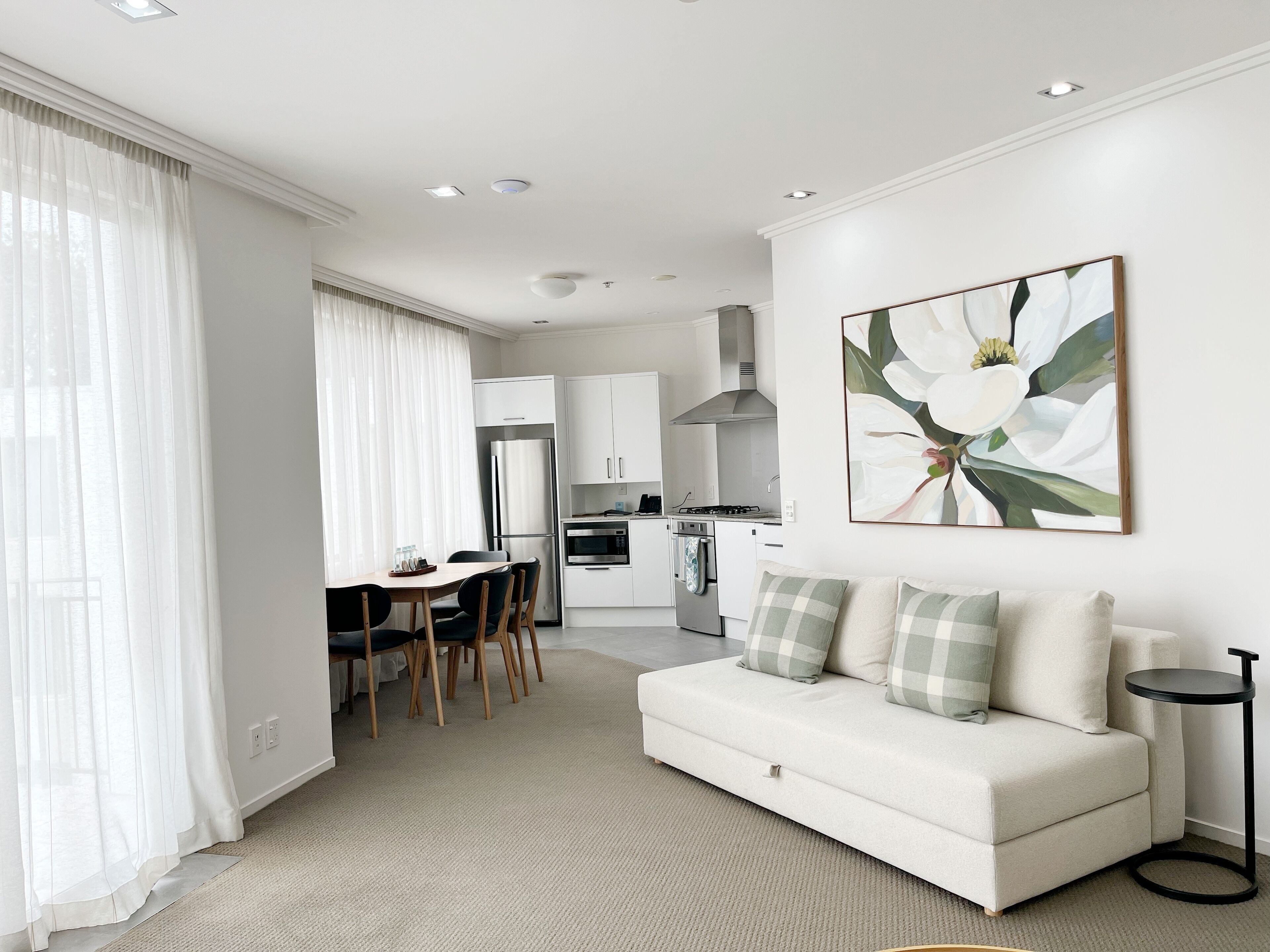 A modern living room with a sofa, a dining table with chairs, and a kitchen in the background.