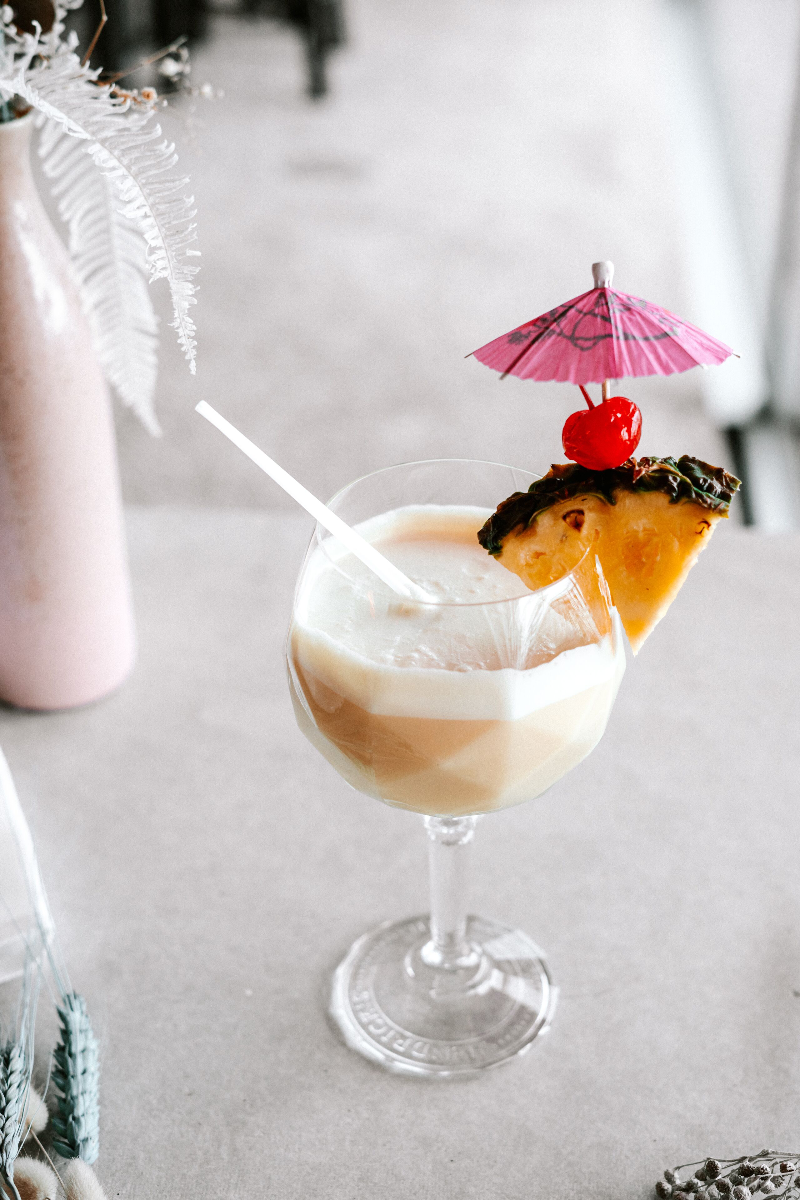 Un cocktail servi dans un verre, avec une paille, une tranche d’ananas et une cerise sur le dessus.