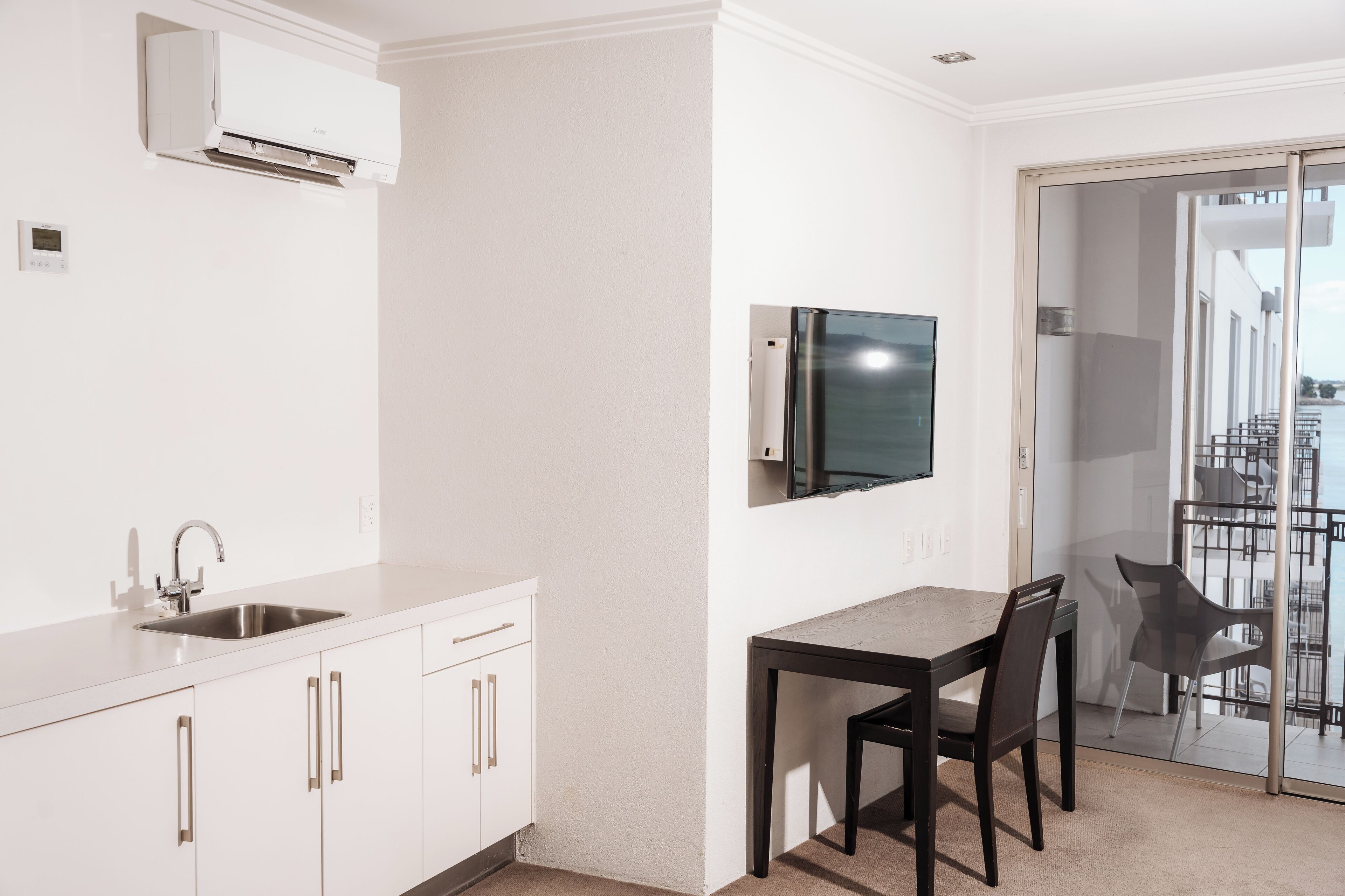 Una cocina moderna con armarios blancos, un lavamanos de acero inoxidable y aire acondicionado integrado.