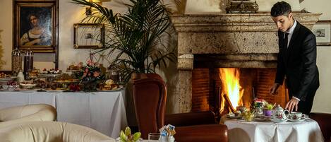 A dining room with a fireplace, a table set for a meal, and a waiter attending to the table.