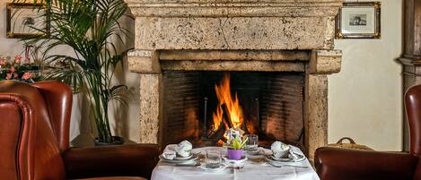 A dining area with a fireplace, leather chairs, a table set for two, and a potted plant.