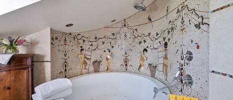 Un baño con una bañera grande, un armario de madera y una pared con mosaicos.