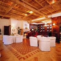 Una habitación amplia con vigas de madera en el techo, una chimenea y varias mesas redondas con sillas.