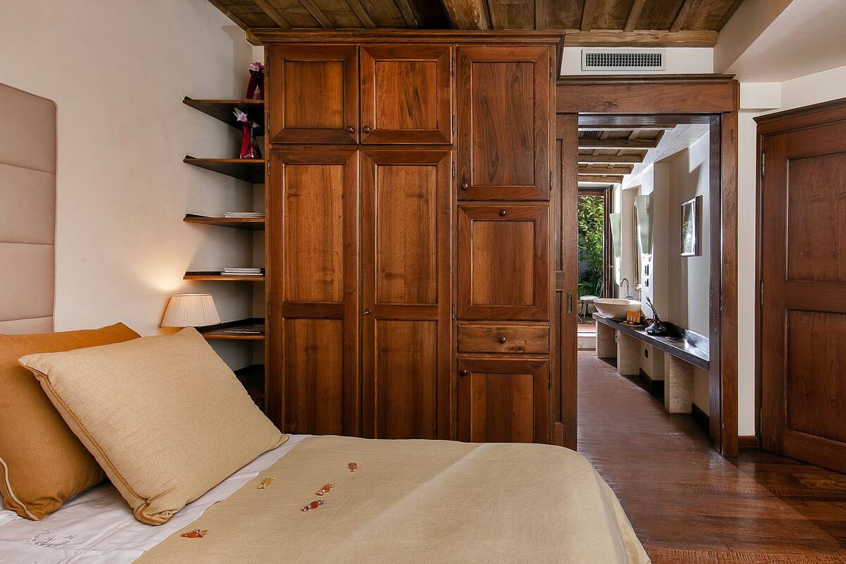 A bedroom with a large wooden wardrobe, a bed with beige bedding, and a nightstand with a lamp.