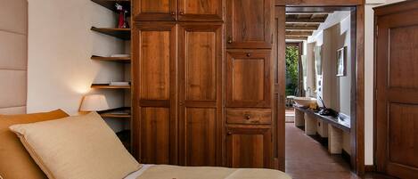 A bedroom with a large wooden wardrobe, a bed with beige bedding, and a nightstand with a lamp.