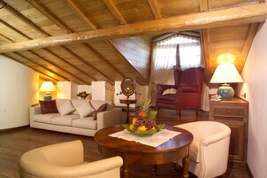 Un salón acogedor con techo de madera, un sofá, dos sillones, una mesita con fruta y una lámpara.