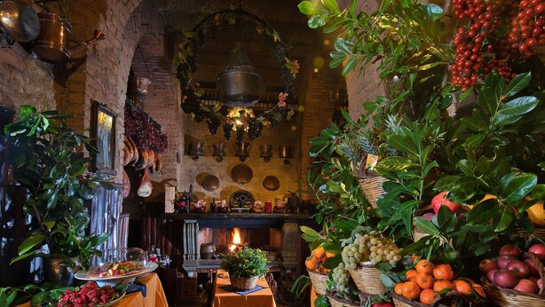 A rustic interior with a brick fireplace, wooden tables, and baskets of fruits and vegetables. - Locanda dello Spuntino (Grottaferrata)