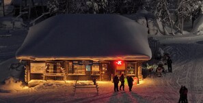 Una cabaña nevada con un letrero de alquiler de esquíes, fachada de madera y un letrero rojo que indica un restaurante o bar.