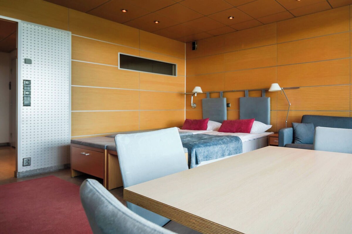 Quarto de hotel com cama, duas mesas de cabeceira, escrivaninha, sofá e tapete vermelho.