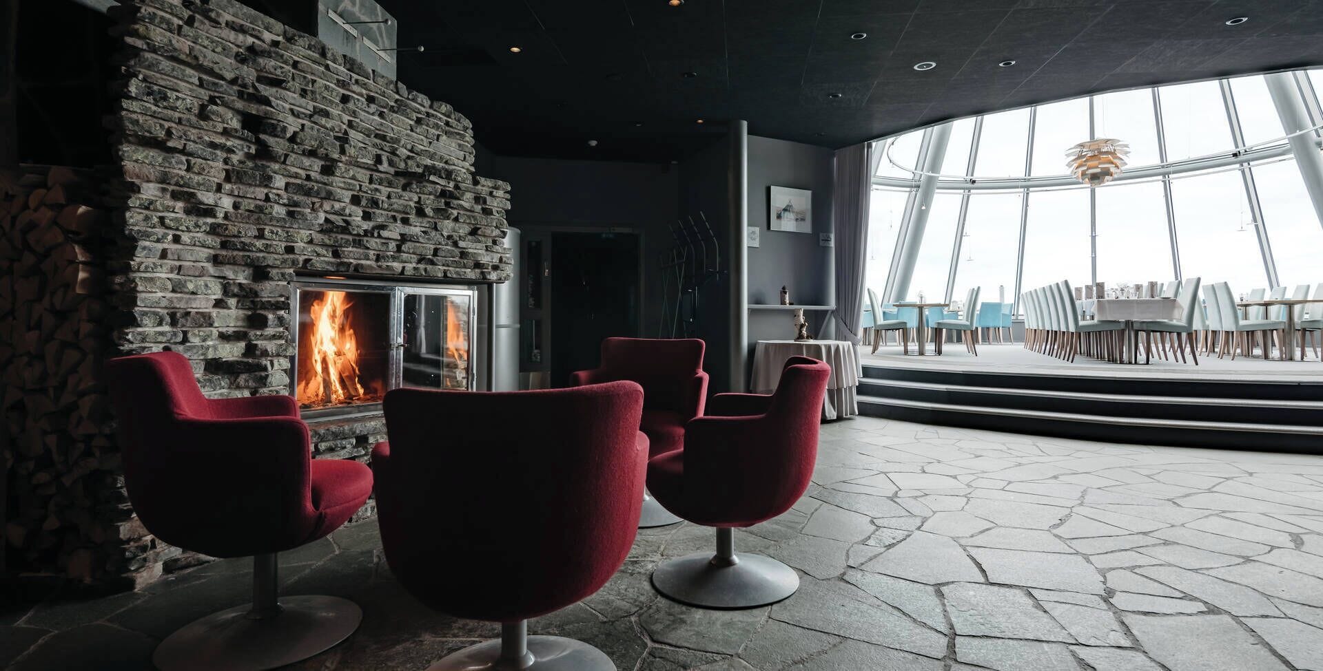 A modern interior with a stone wall fireplace, red chairs, and a view of the outdoors through large windows.