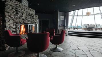 A modern interior with a stone wall fireplace, red chairs, and a view of the outdoors through large windows.