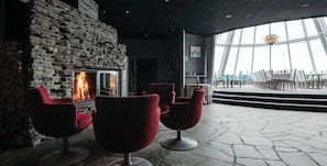 Un interior moderno con chimenea de piedra, sillas rojas y vistas al exterior a través de amplios ventanales.