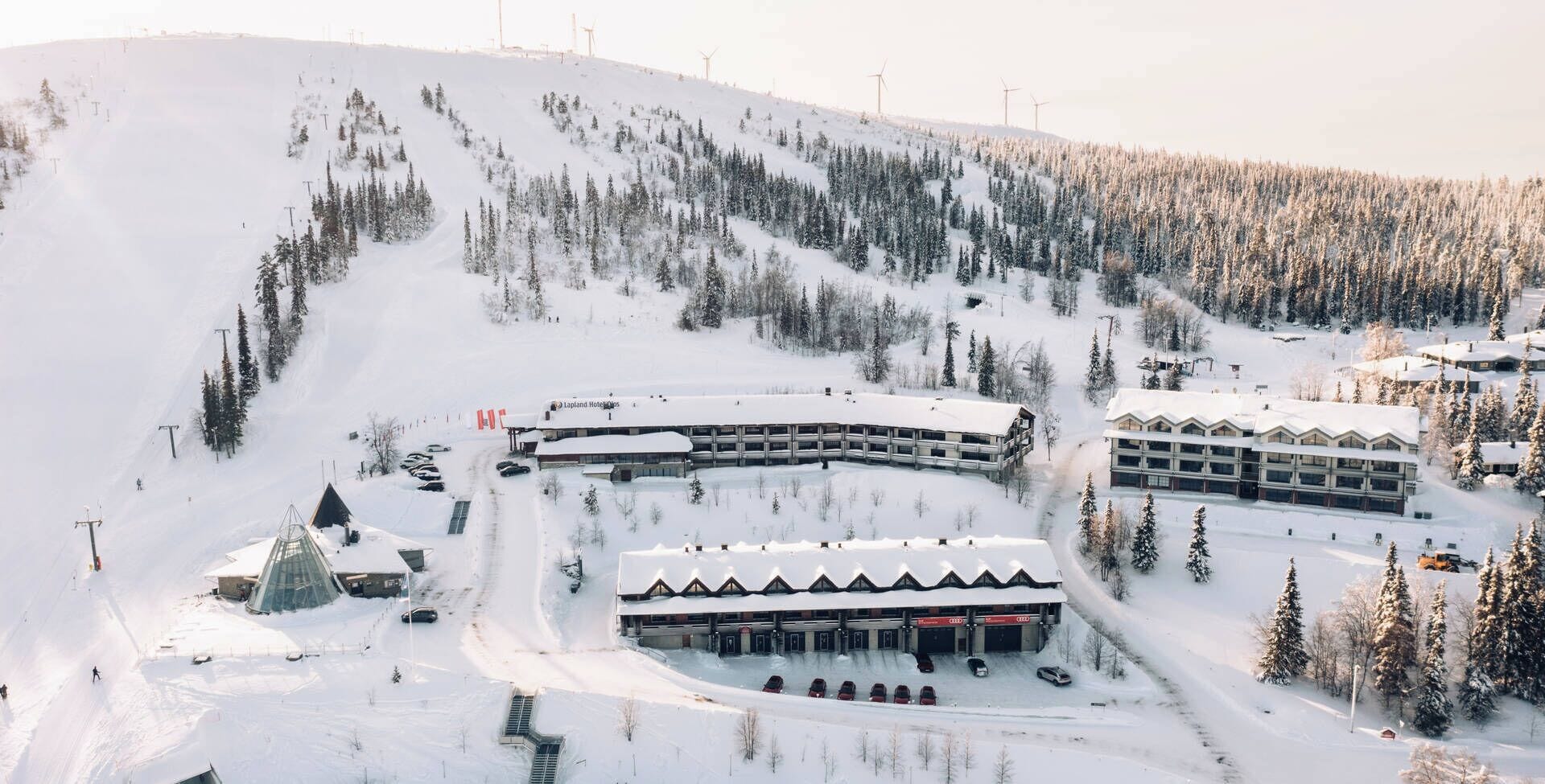 A snow-covered ski resort with multiple buildings, including a hotel and a parking area.