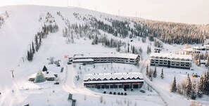 A snow-covered ski resort with multiple buildings, including a hotel and a parking area.