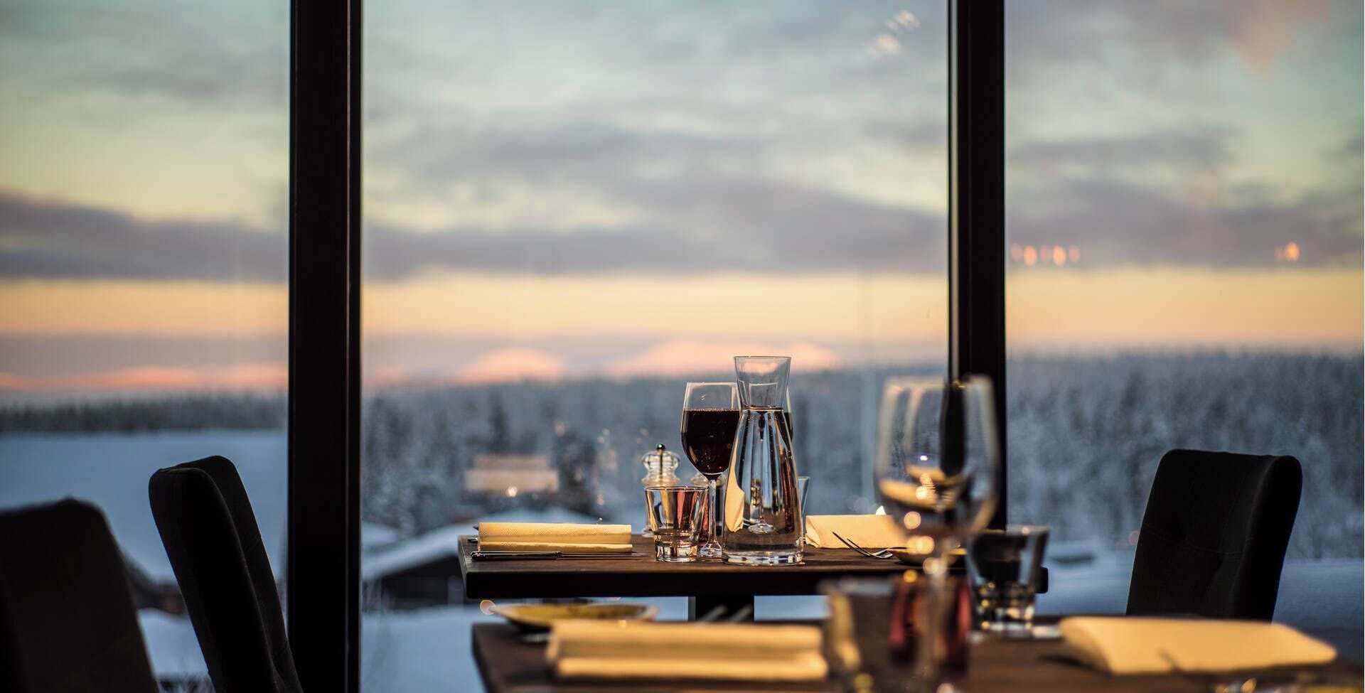 A table set for dining with a view of a snowy landscape through large windows.