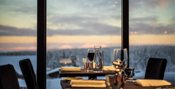 A table set for dining with a view of a snowy landscape through large windows.