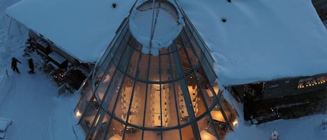 Un bâtiment enneigé, surmonté d’une structure circulaire en verre au centre, le tout entouré de neige.