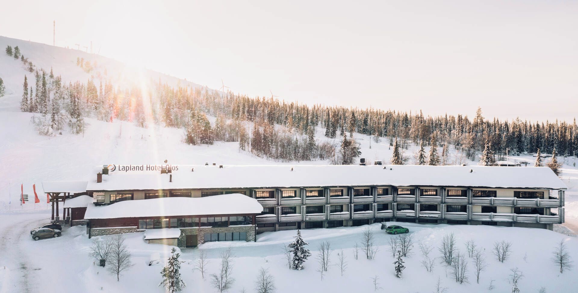 A hotel with a snow-covered roof, a lobby area, and a parking lot with a green car.