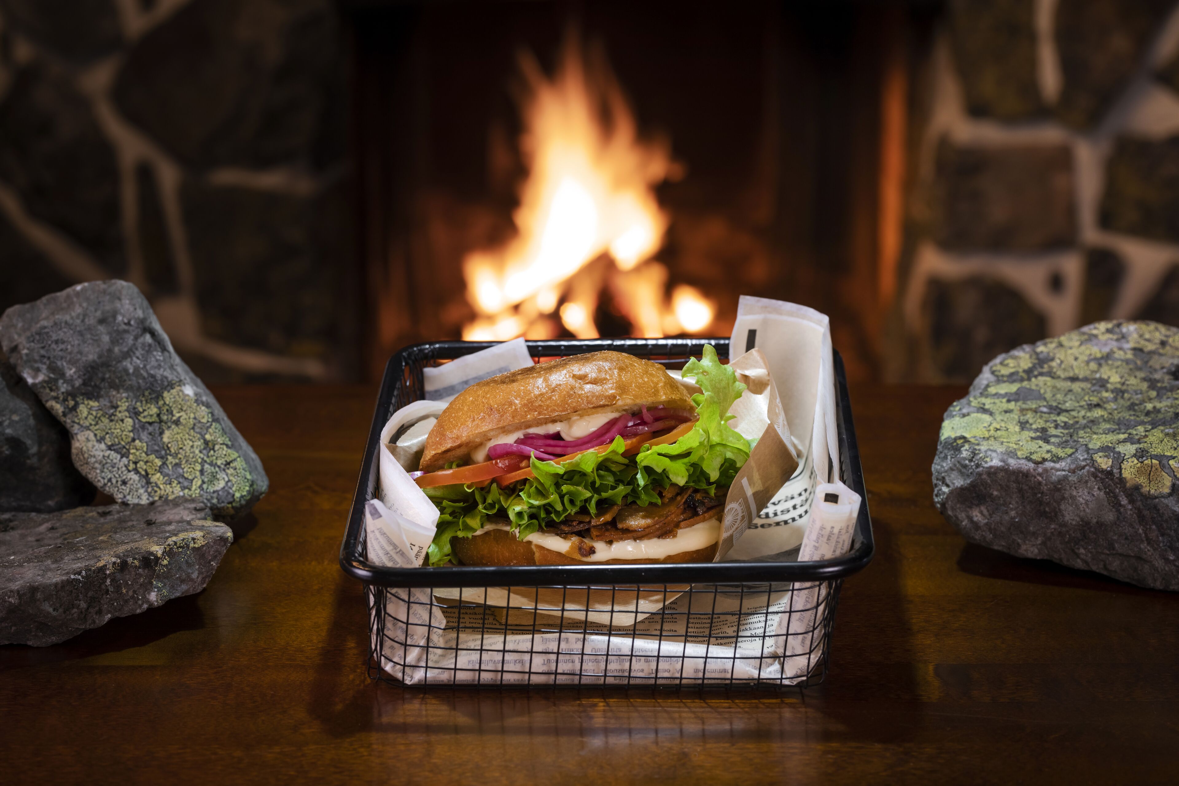 Un panier contenant un sandwich et des couverts, posé sur une table en bois, avec une cheminée en pierre en arrière-plan.