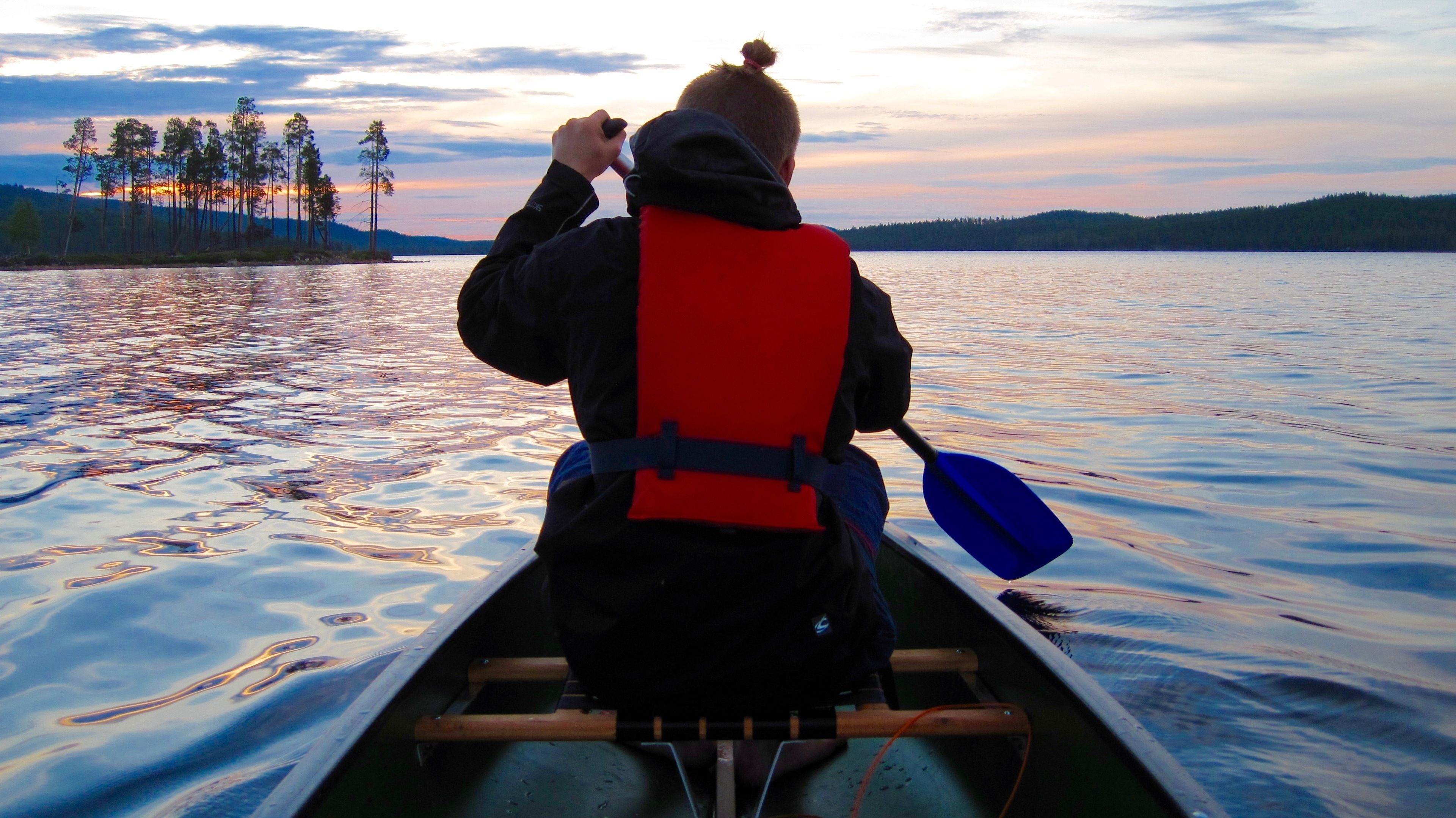 Una persona en un canoa sobre un lago tranquilo con árboles al fondo.