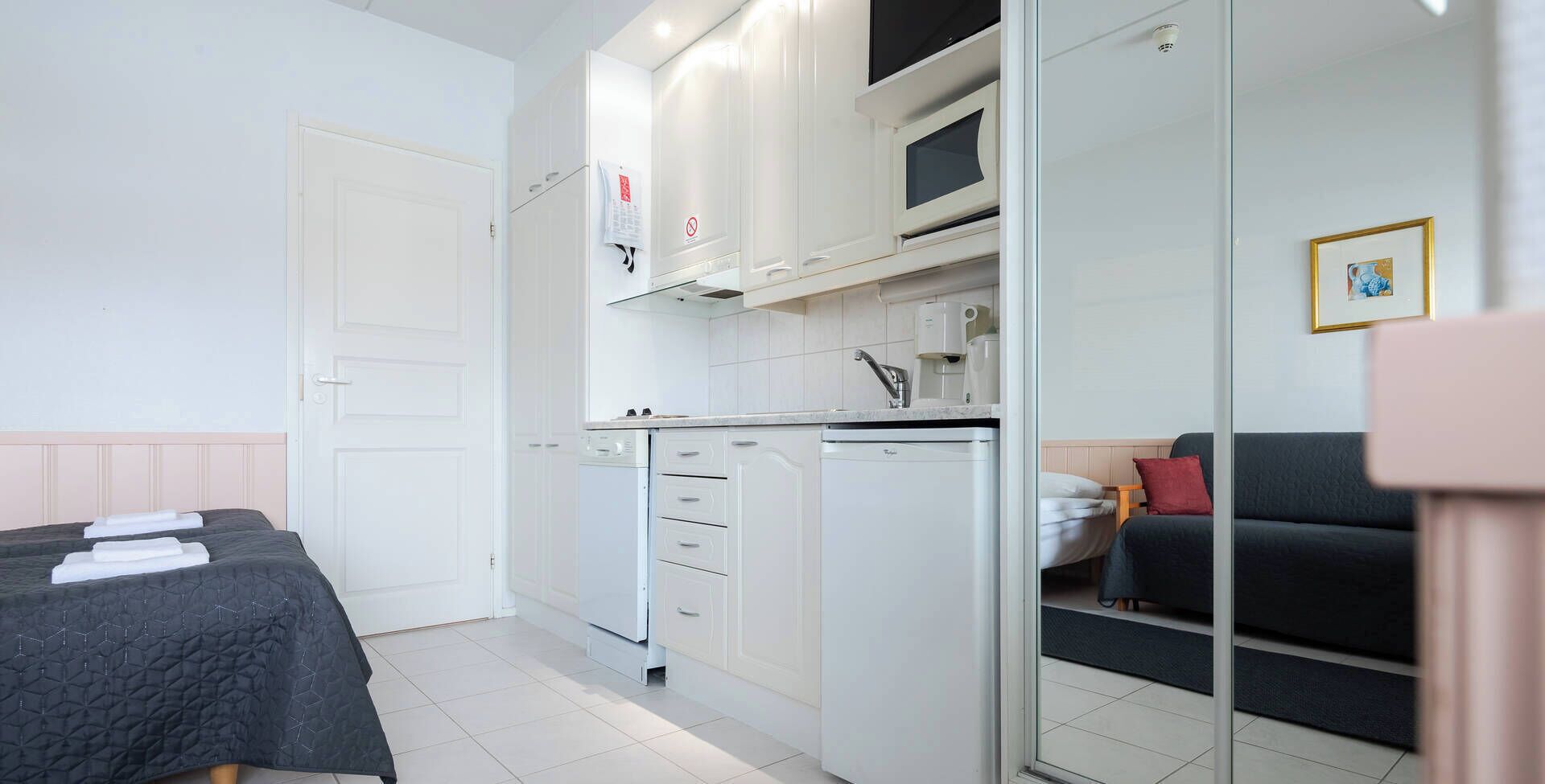 A compact room with a bed, kitchenette, and a seating area.