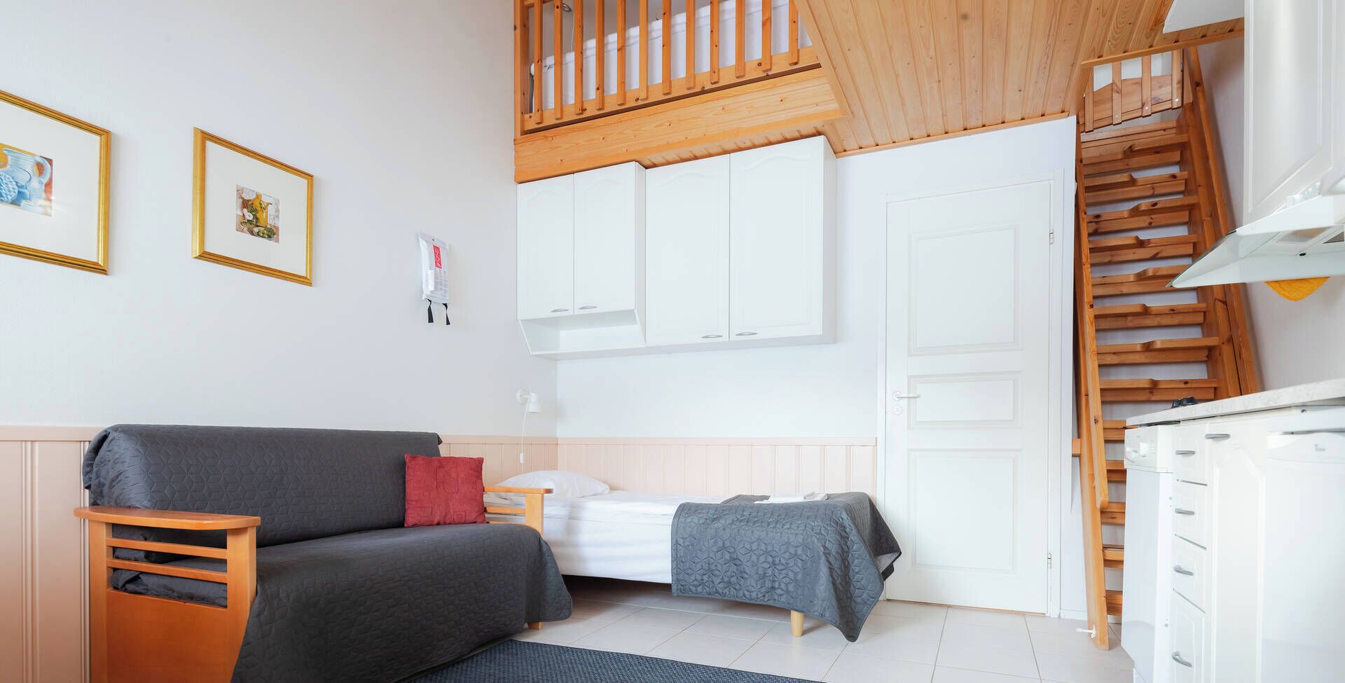 A compact bedroom with a bed, a small bedside table, a wooden bench, a wardrobe, and a staircase.