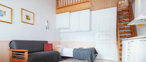 A compact bedroom with a bed, a small bedside table, a wooden bench, a wardrobe, and a staircase.