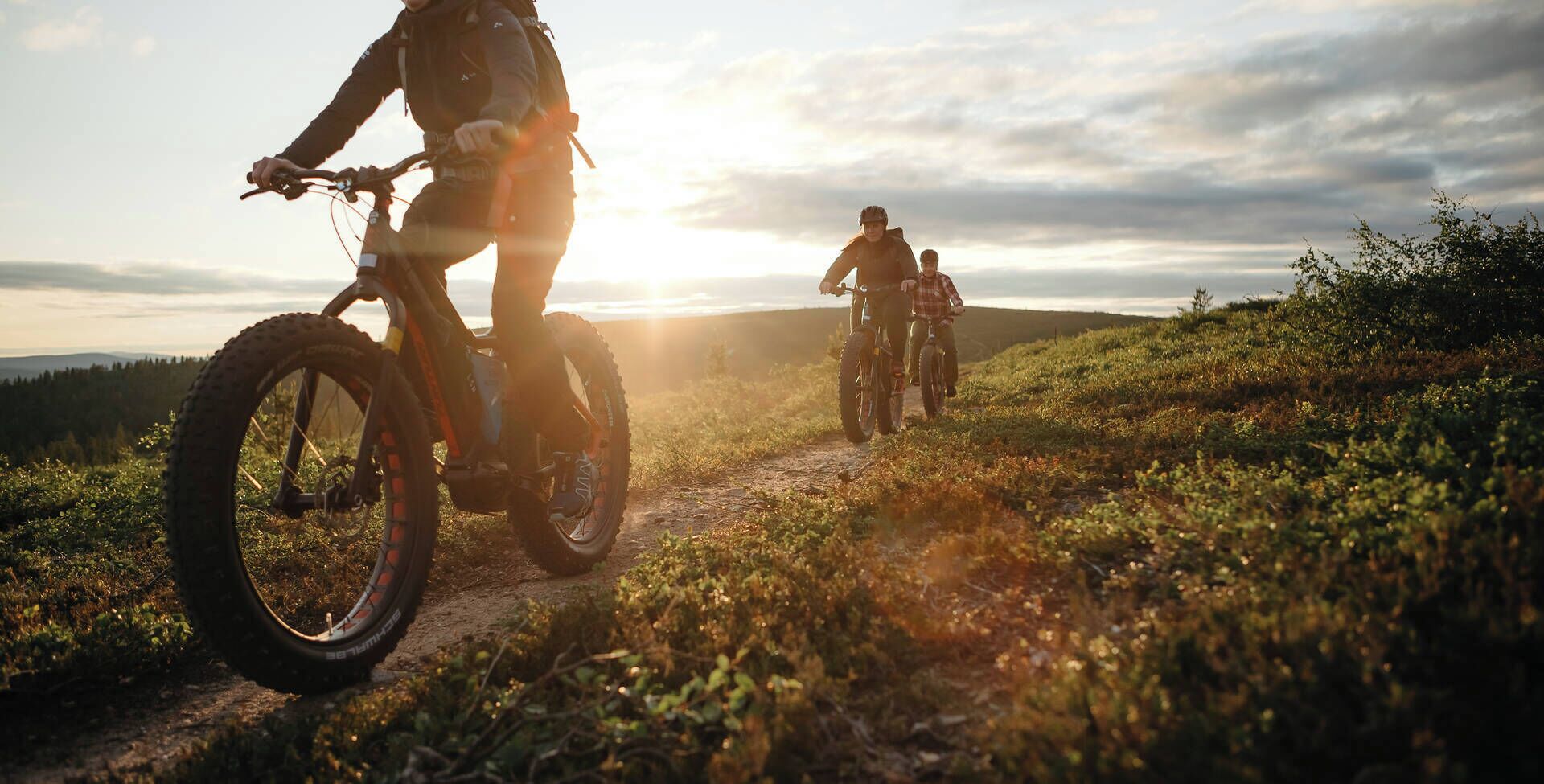 Dos ciclistas de montaña en un sendero de tierra, con una vista panorámica de un bosque y colinas al fondo.