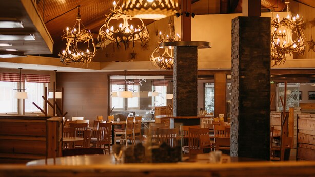A restaurant interior with wooden furniture, chandeliers, and a stone pillar.