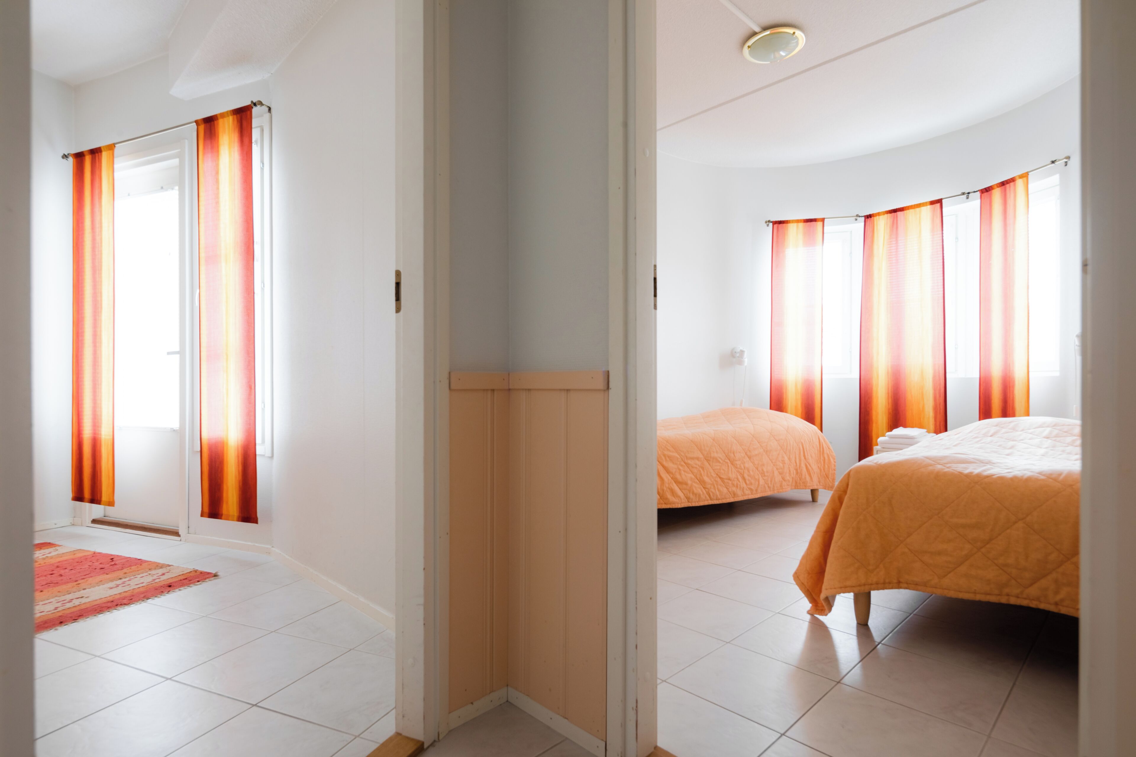 Une chambre d’hôtel avec un lit, une fenêtre avec des rideaux, une porte et un sol carrelé.