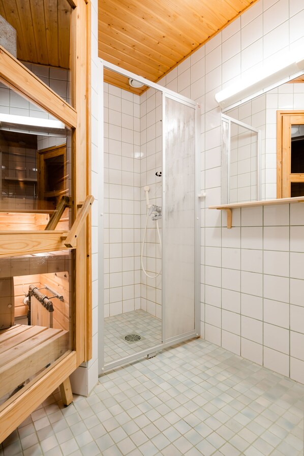 Un interior de madera con cabina de ducha de vidrio, paredes con azulejos y un banco de madera.