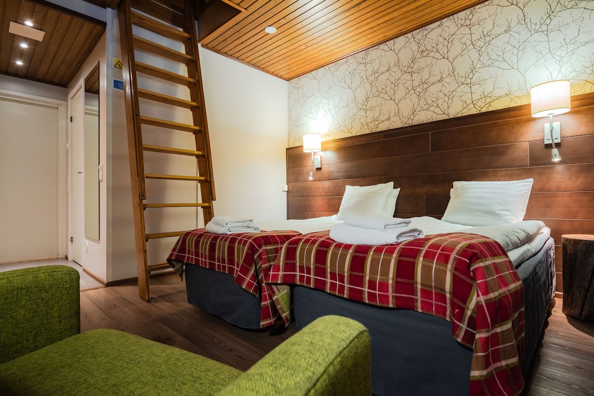 Een hotelkamer met twee bedden, een houten trap, groene stoelen en een houten plafond.