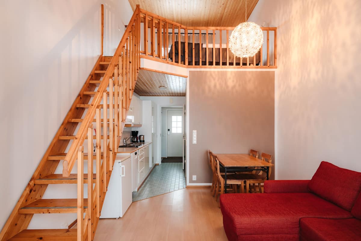 Een ruime woonkamer met een houten trap, een eettafel en een rode bank.