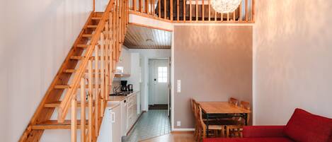 A spacious living area with a wooden staircase, a dining table, and a red sofa.