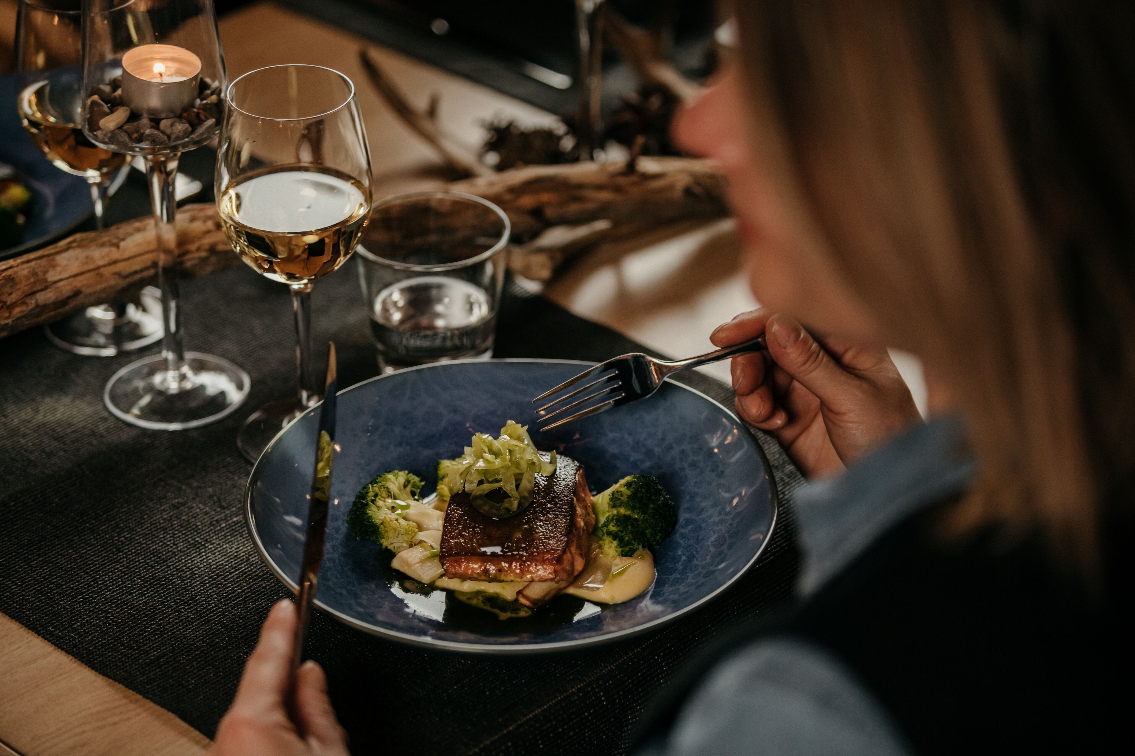 Una mesa de comedor con un plato de comida, una copa de vino blanco y una vela.