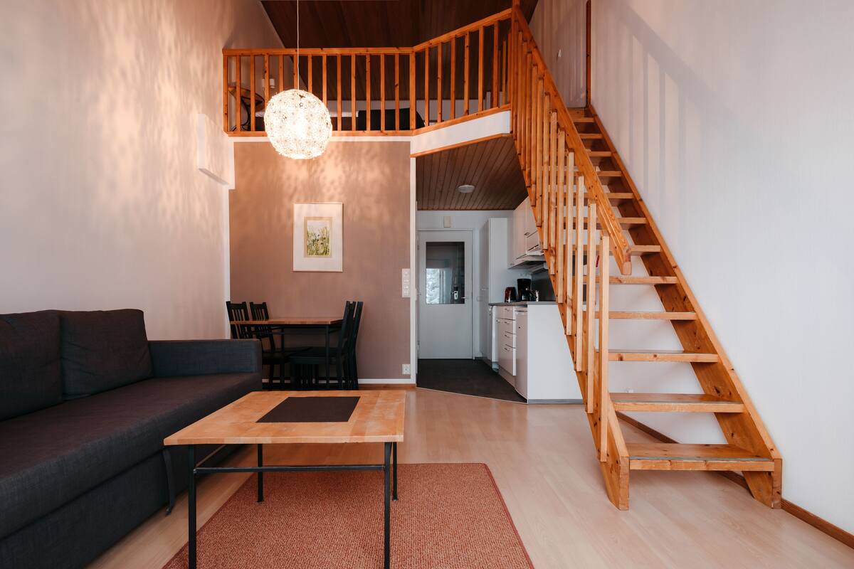 Een moderne woonkamer met een houten trap, een eethoek en een keuken.