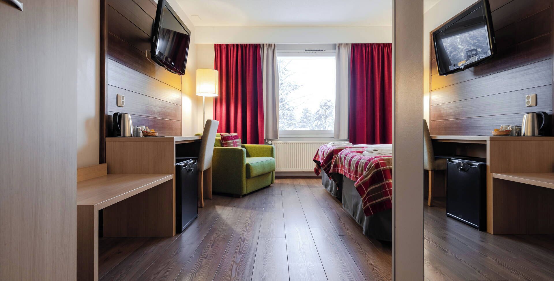 A compact hotel room with a bed, a desk, a chair, a TV, and a window with curtains.