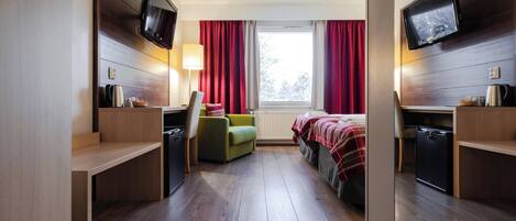 A compact hotel room with a bed, a desk, a chair, a TV, and a window with curtains.
