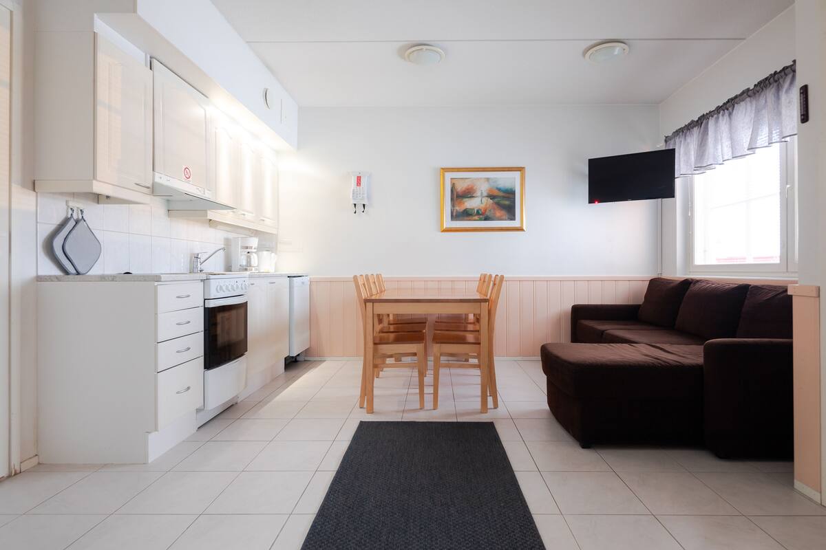 Een moderne keuken met witte kasten, een eettafel met stoelen, een bruine bank en een schilderij aan de muur.
