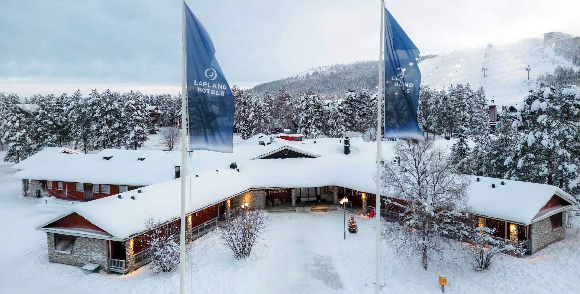 A hotel with a snow-covered landscape, multiple flags, and a mountainous backdrop.