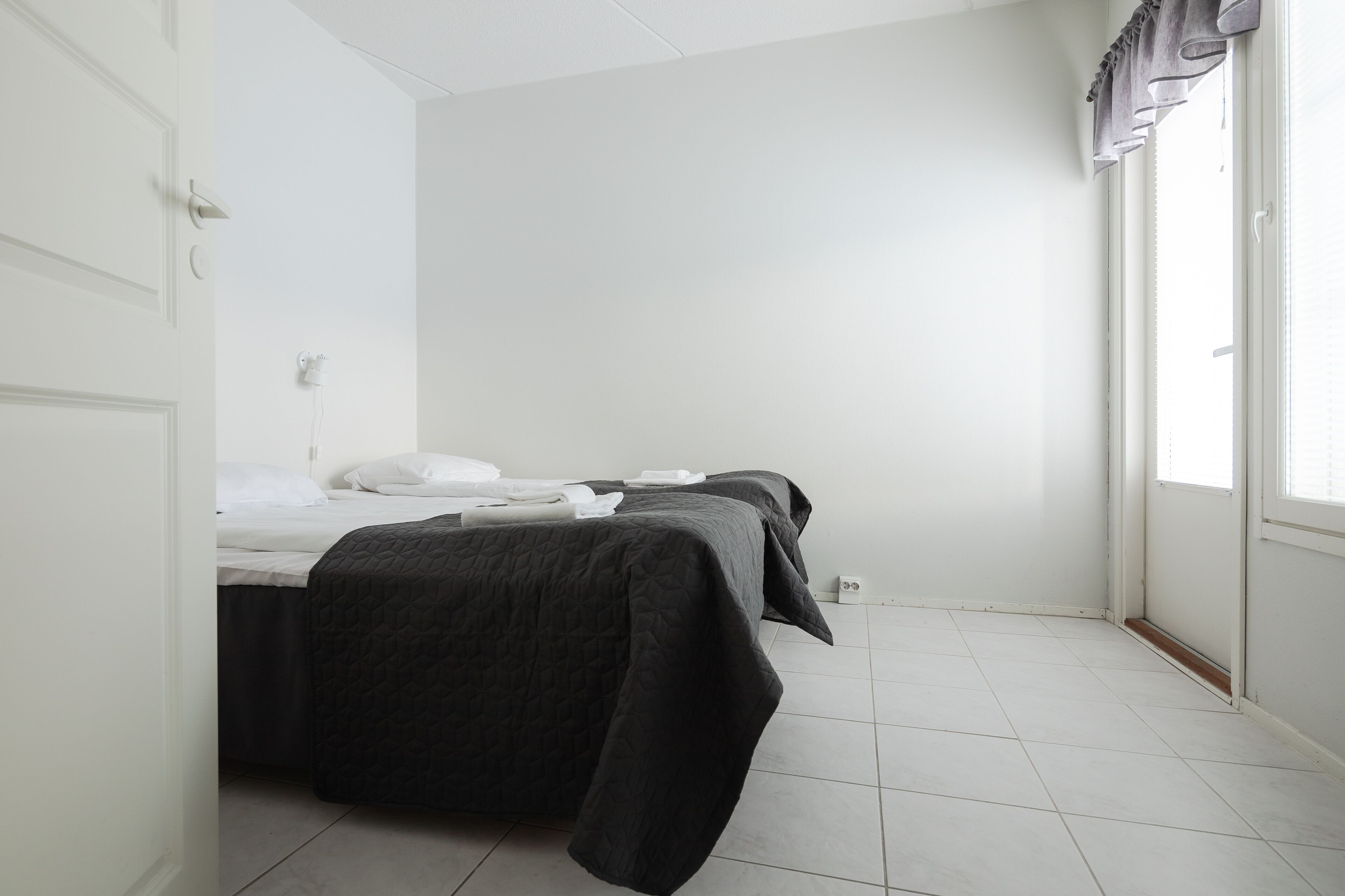 Una habitación con dos camas, paredes blancas y un ventanal con cortinas.