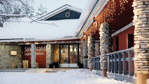 A hotel with stone pillars, a snow-covered roof, and a sign for 'Sirk Lapla Hotels'.