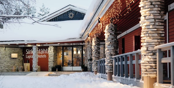 A hotel with stone pillars, a snow-covered roof, and a sign for 'Sirk Lapla Hotels'.