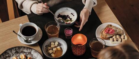 Una mesa de comedor con diversos alimentos y bebidas, incluyendo un tazón de yogur con frutos rojos, una tostada con mermelada y una taza de café.