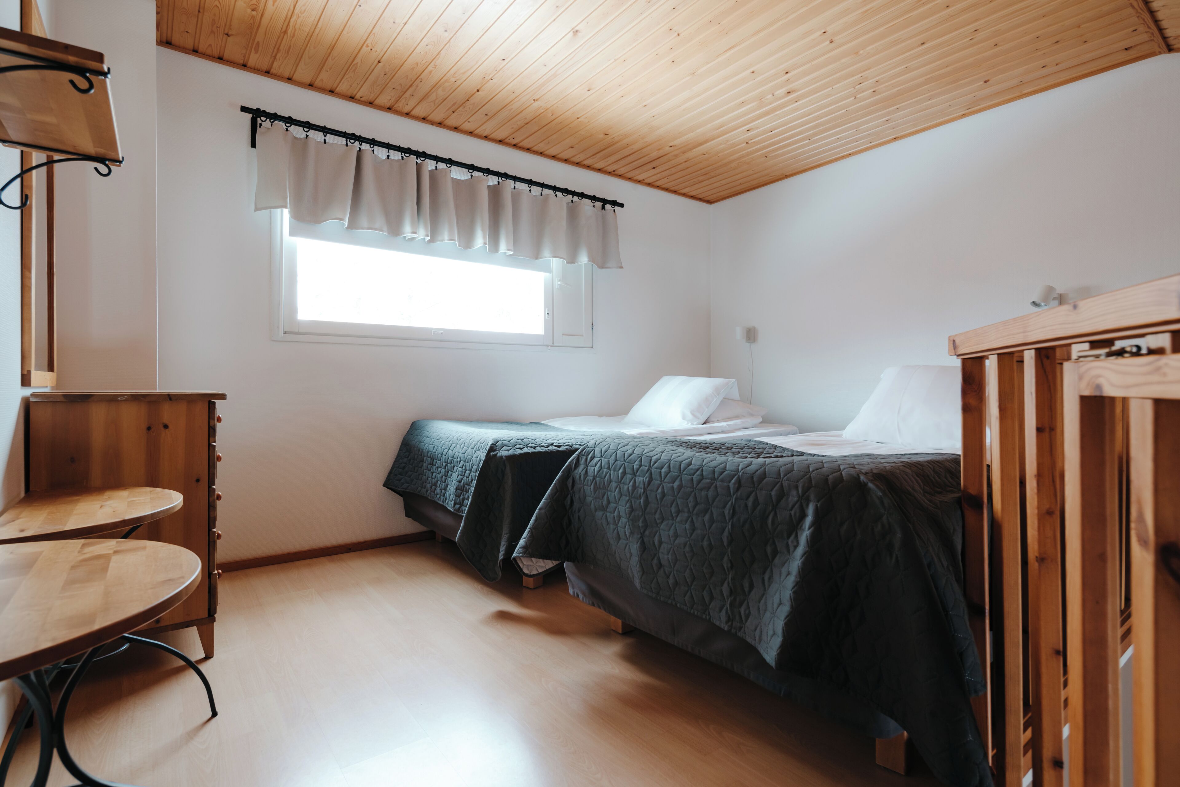 Une petite pièce agréable, dotée d’un lit simple, d’une table en bois et d’une fenêtre avec un rideau.