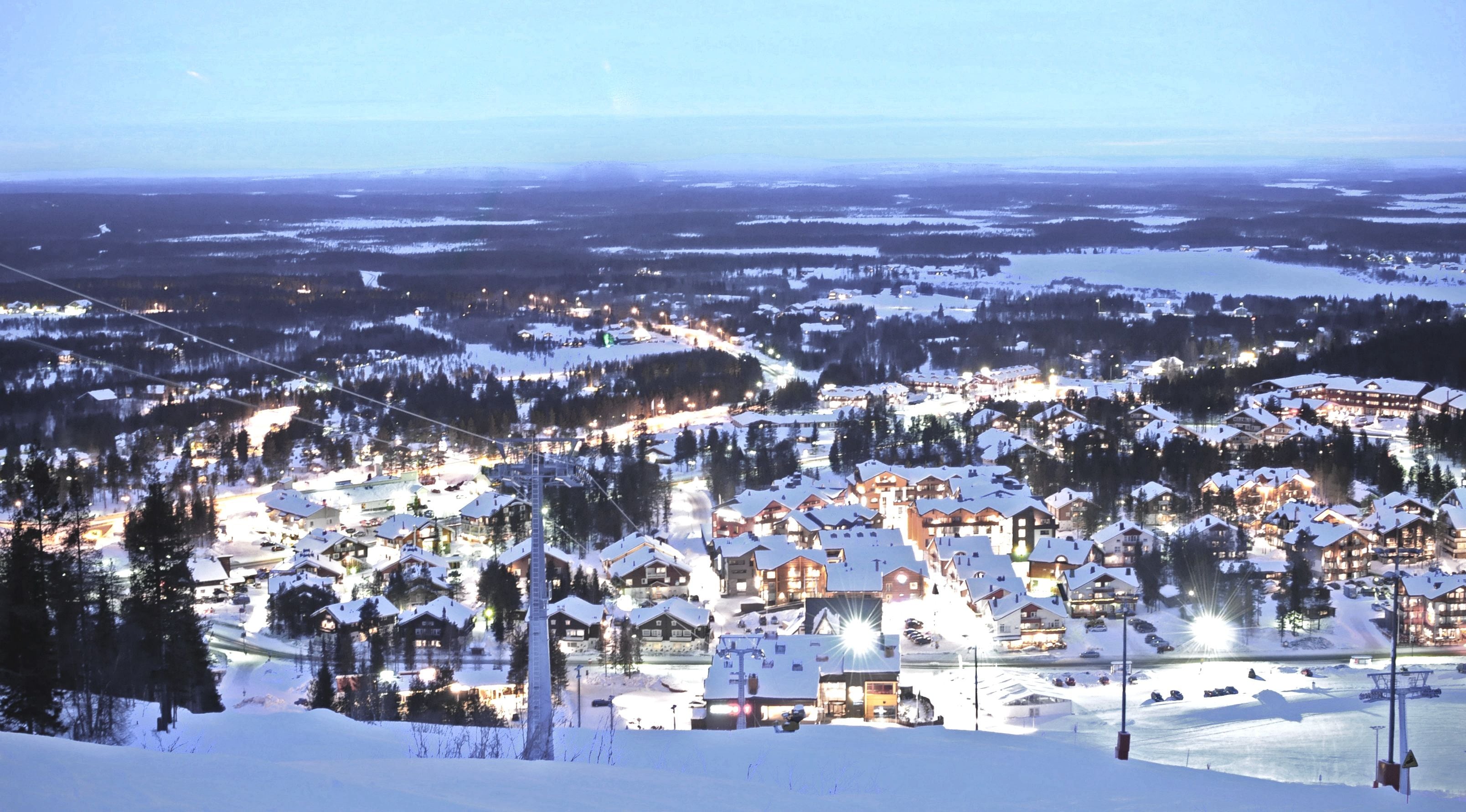 A snow-covered town with multiple buildings, including a prominent hotel with a ski lift visible in the background.