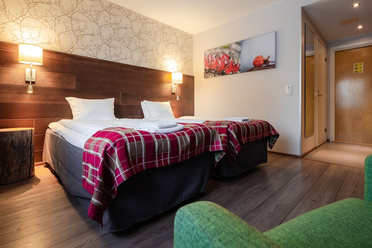 Een hotelkamer met een groot bed, twee bedlampen, een houten hoofdbord, een groene fauteuil en een schilderij aan de muur.