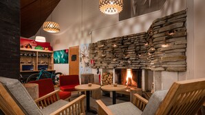 A cozy lounge area with wooden furniture, a stone wall fireplace, and a bicycle in the background.
