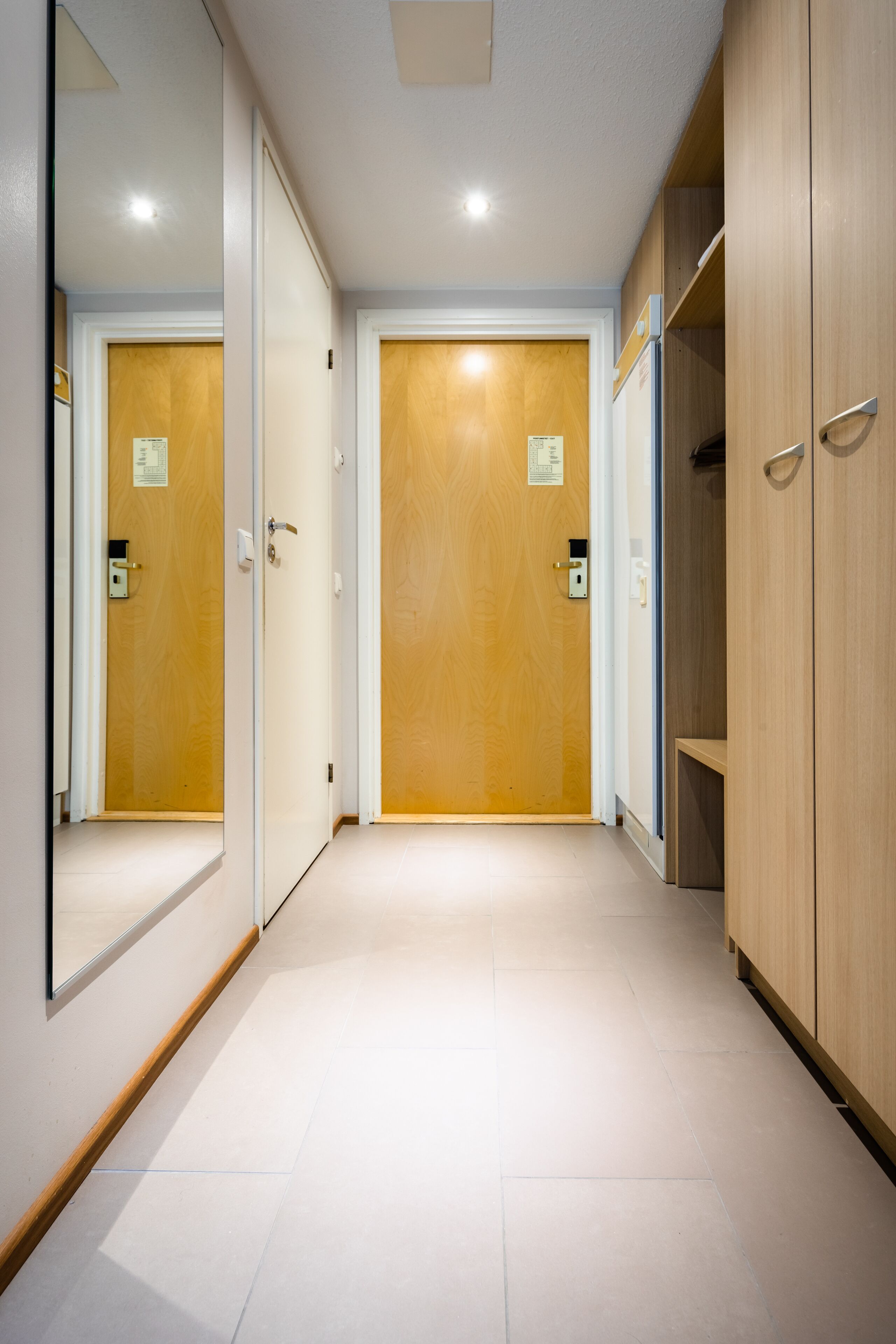 A hallway with wooden doors, a mirror, and a light switch on the wall.